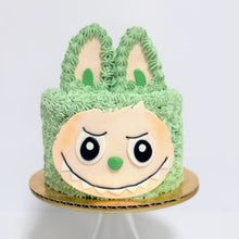Load image into Gallery viewer, Green frosted cake with a face design on a white background
