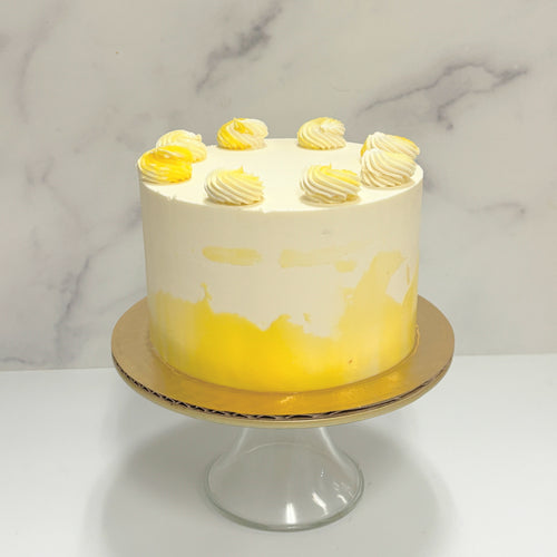 Photo shows a small round cake covered in ivory buttercream with yellow details on the sides and white and yellow piped rosettes on top.