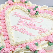 Load image into Gallery viewer, Photo shows a tall heart shaped cake frosted with white buttercream and adorned with intricate buttercream piped swags, rosettes, shell borders and leaves in shades of light pink, ivory and green. Inscription on the center top of the cake reads &#39;Happy Birthday Malina&#39; in pink piped buttercream.
